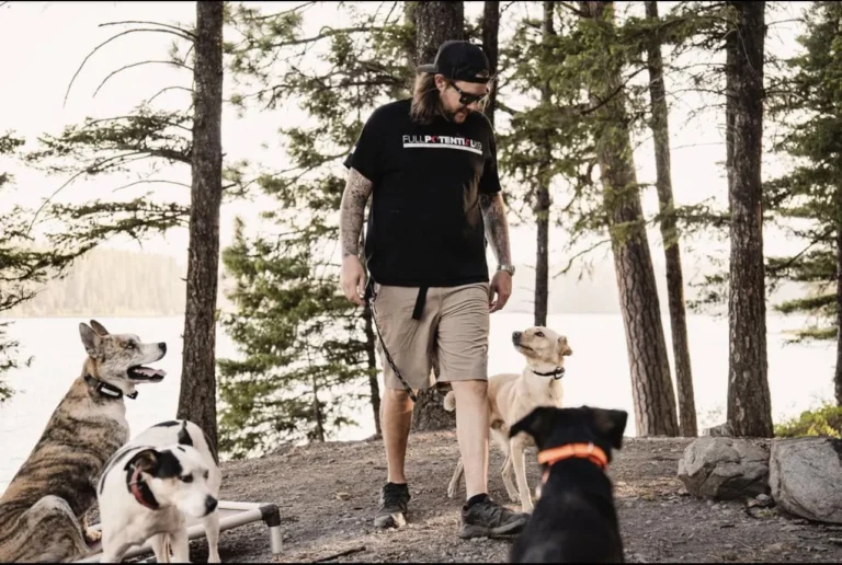 A Full Potential K9 trainer walking calmly with several dogs along a forested lakeshore